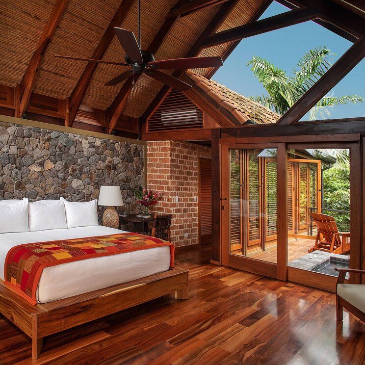 Luxuriöses Zimmer im Hotel Amor Arenal in La Fortuna, Costa Rica, mit Holzboden, Natursteinwand, großen Panoramafenstern und Zugang zur privaten Terrasse im tropischen Regenwald.