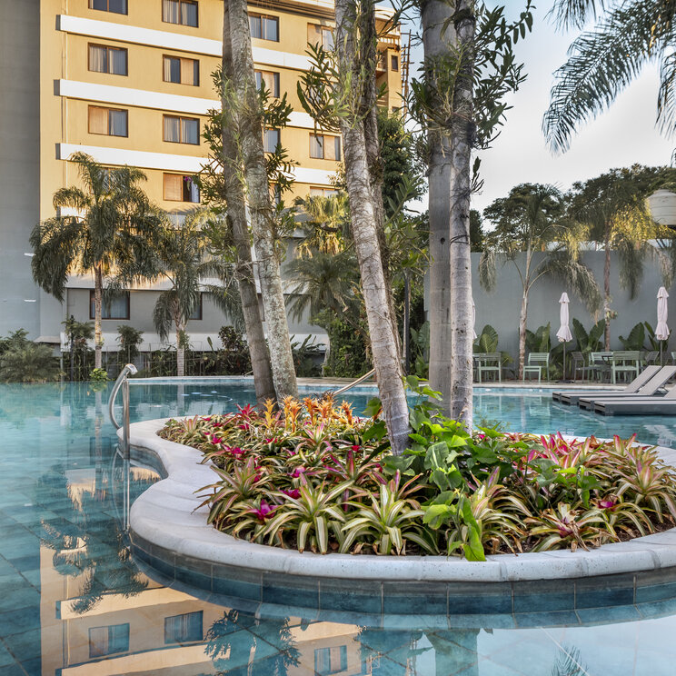 Swimmingpool mit bepflanzter Insel und Palmen vor einem Hotelgebäude in Lateinamerika.