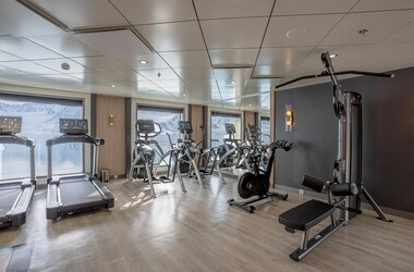 Der moderne Fitnessraum an Bord der Ocean Albatros mit Laufbändern und Trainingsgeräten direkt vor den Panoramafenstern.