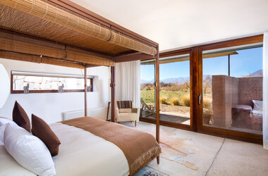 Schlafzimmer mit Holz-Himmelbett und grosser Glasfront zur Terrasse mit Blick auf die Wüste von Chile.