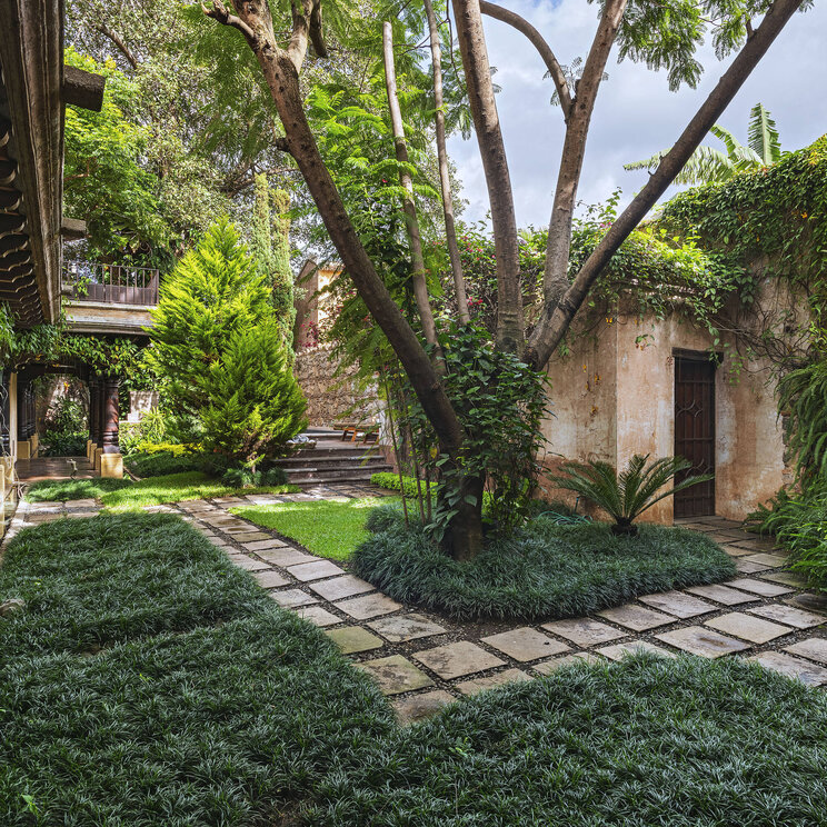 Grüner Innenhof im El Convento Boutique Hotel in Antigua, Guatemala, mit gepflegten Gartenwegen, Schatten spendenden Bäumen und kolonialem Arkadengang.