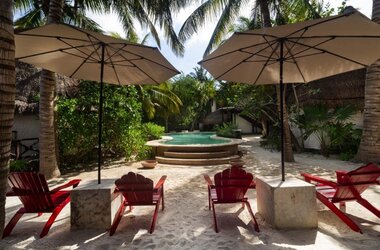 Außenpool umgeben von Palmen, Sonnenschirmen und roten Holzstühlen auf Holbox, Mexiko