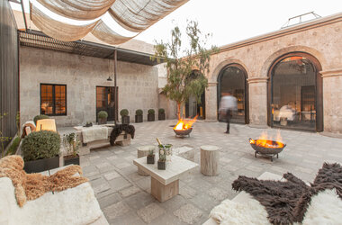 Beleuchteter Innenhof bei Daemmerung mit Feuerschalen, Sitzgelegenheiten und Fellen im CIRQA Hotel Arequipa.