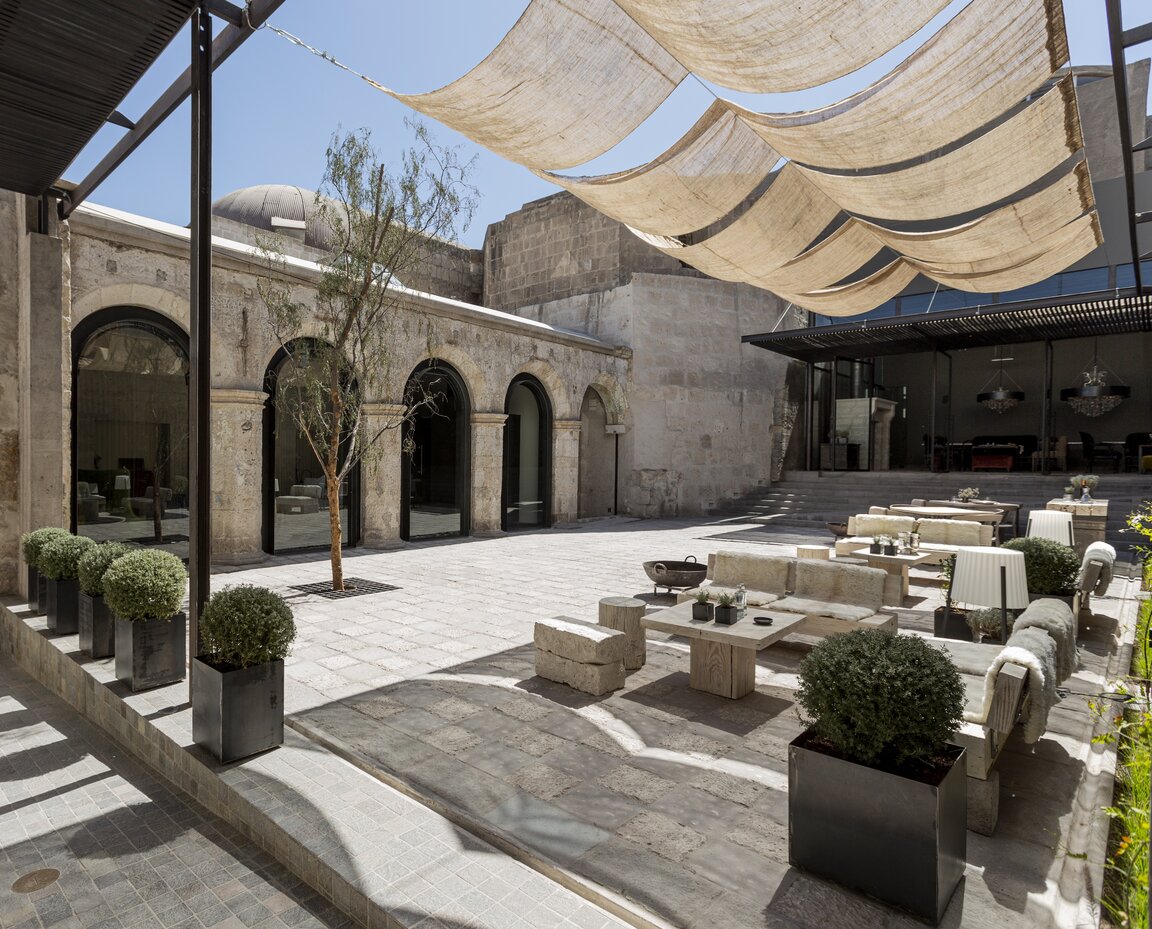 Gepflasterter Innenhof mit Steinbaenken, Topfpflanzen und hellen Sonnensegeln im CIRQA Hotel Arequipa, Peru.