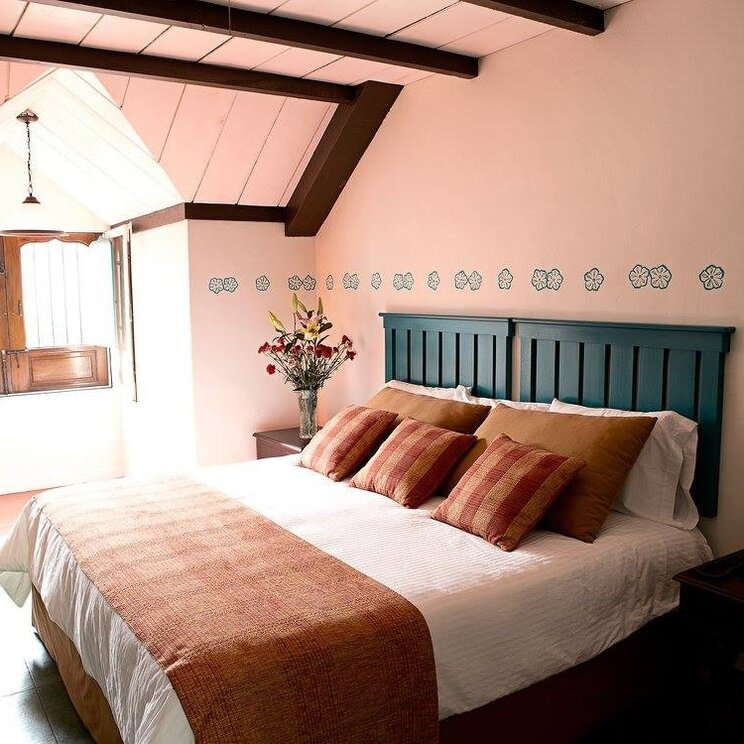 Suite mit Doppelbett, Wanddekoration, dunklen Deckenbalken und geoeffnetem Holzfenster im Hotel Isla de Flores.