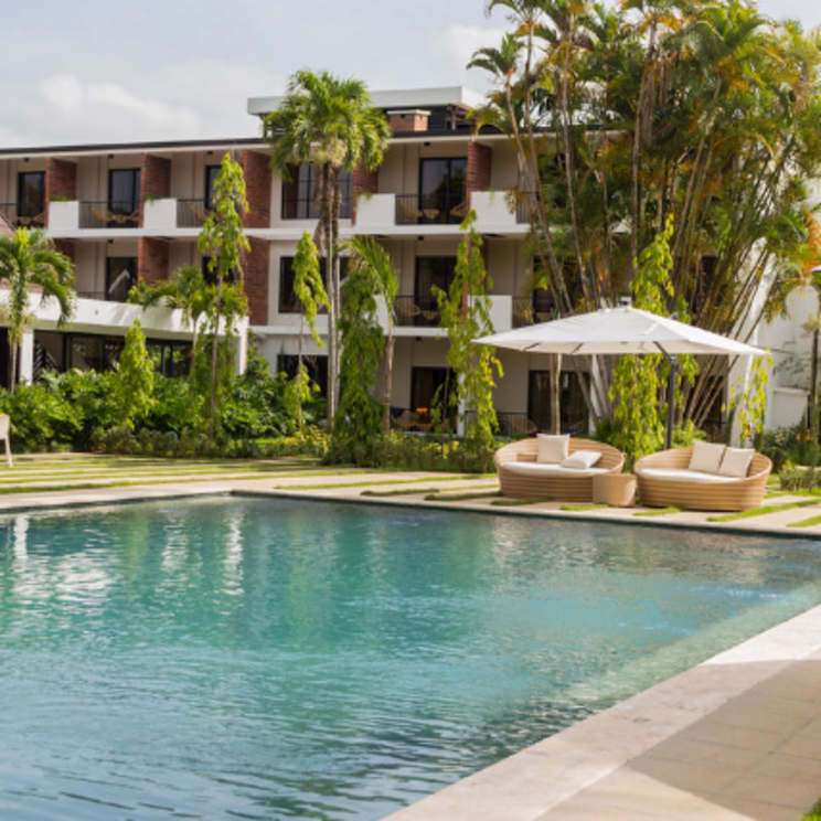 Poolbereich im Hotel Pinar Dorado in Jarabacoa, Dominikanische Republik, umgeben von tropischer Vegetation, modernen Liegen und dem Haupthaus im Hintergrund.