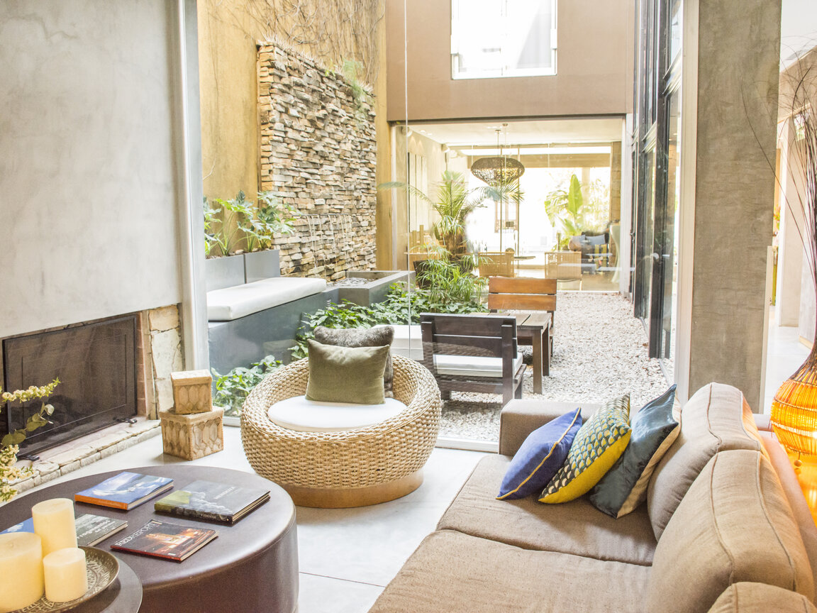Lounge mit Sofa und Kamin neben einem verglasten Innenhof mit Springbrunnen im Mine Hotel in Buenos Aires.