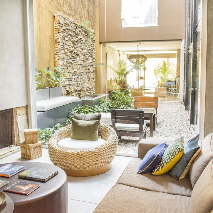 Lounge mit Sofa und Kamin neben einem verglasten Innenhof mit Springbrunnen im Mine Hotel in Buenos Aires.