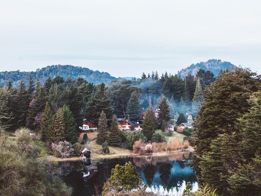 Idyllische Holzhäuser und dichte Nadelwälder an einem ruhigen Seeufer nahe San Carlos de Bariloche in Patagonien, Argentinien
