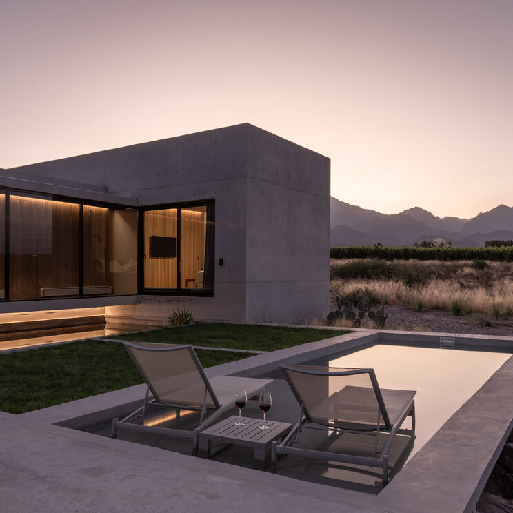 Moderne Betonvilla in Argentinien mit Pool, Sonnenliegen und Bergblick in der Abenddämmerung.