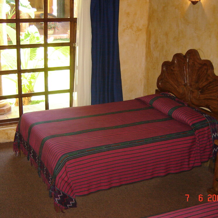 Einzelbett mit lila gestreifter Decke vor großem Fenster zum Innenhof im Hotel Casa Mexicana, Mexiko.