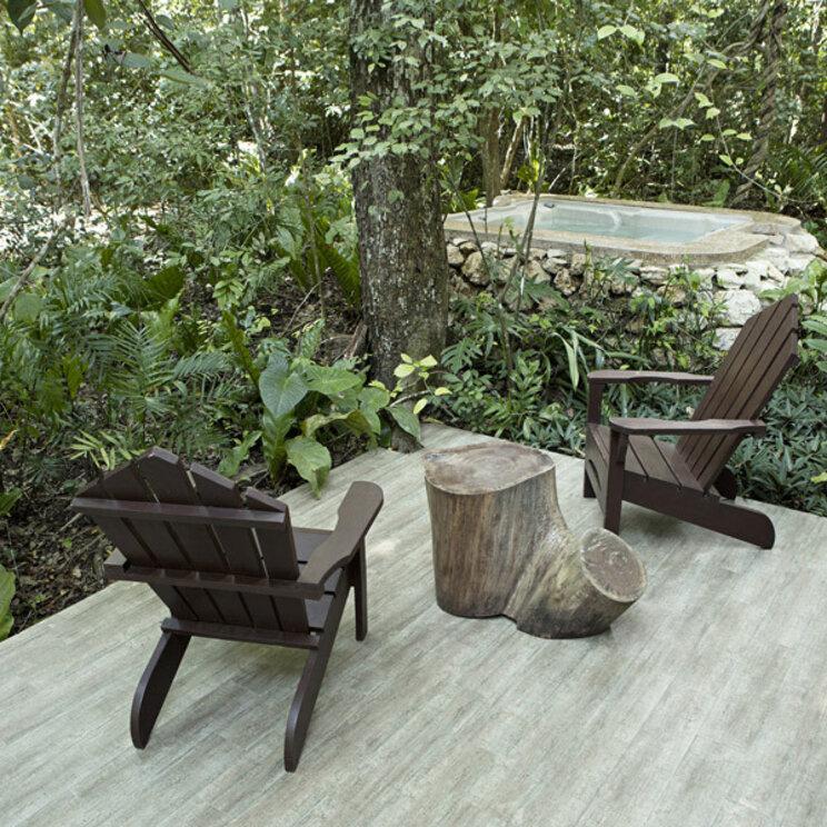 Terrasse der Suite Ortiz mit zwei Holzstühlen und einem in Stein gefassten Whirlpool im Wald von Tikal.