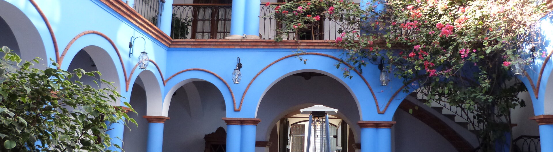 Kolonialer Innenhof in Sucre mit blauen Säulen, Rundbögen, schmiedeeisernen Balkonen und Sitzgruppen in Bolivien.