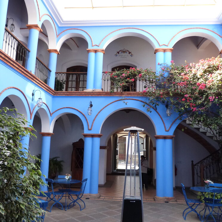 Kolonialer Innenhof in Sucre mit blauen Säulen, Rundbögen, schmiedeeisernen Balkonen und Sitzgruppen in Bolivien.