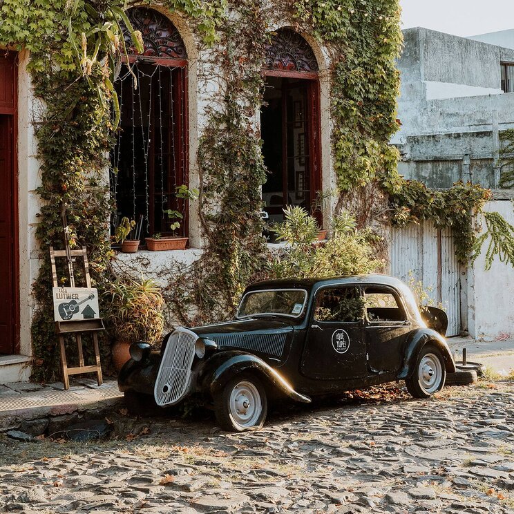 Schwarzer Oldtimer steht auf Kopfsteinpflaster vor einem pflanzenbewachsenen Haus in Uruguay