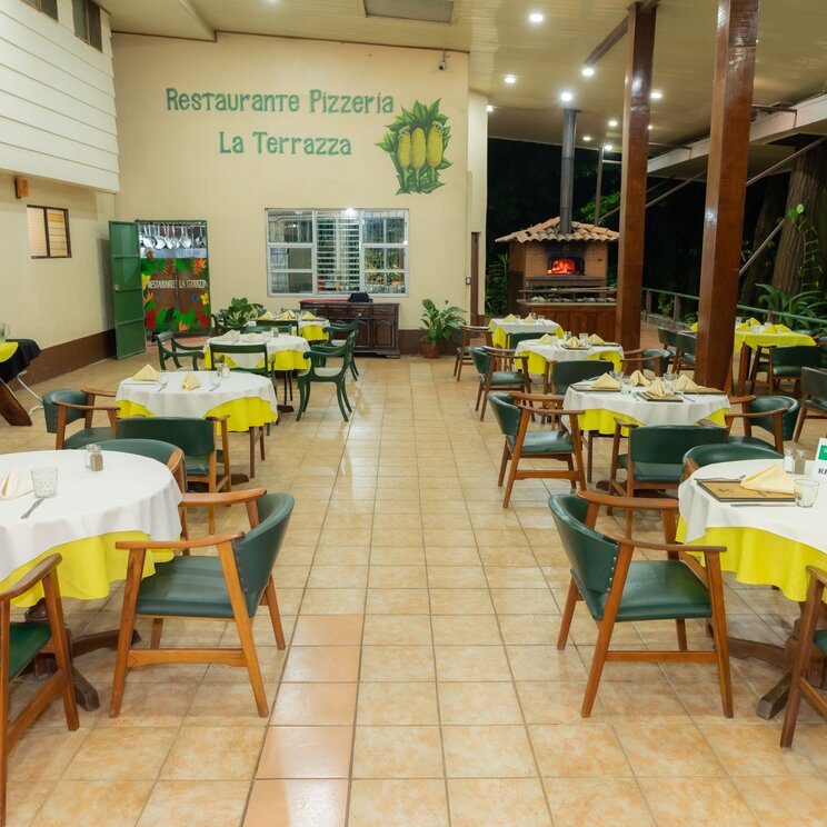 Innenansicht des Restaurants Pizzeria La Terrazza in der Selva Verde Lodge mit eingedeckten Tischen und Stuehlen.