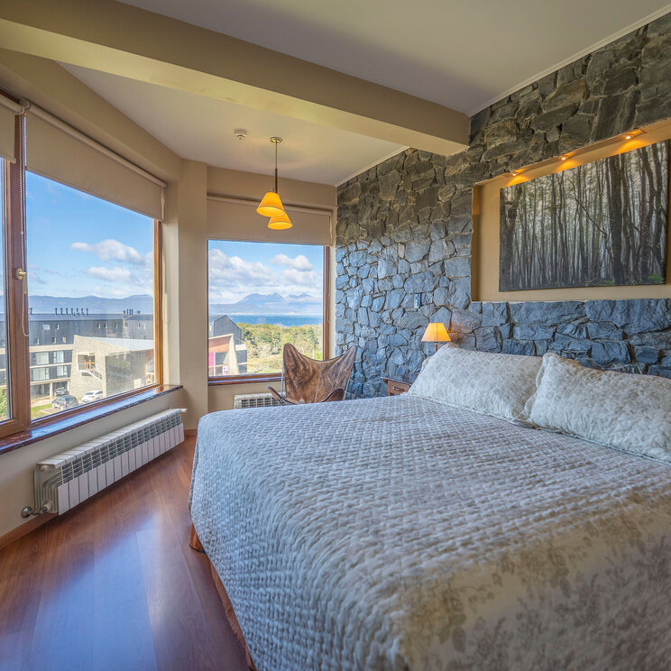 Superior-Doppelzimmer im Hotel Tierra de Leyendas in Ushuaia mit Natursteinwand, Kingsize-Bett und Panoramablick.