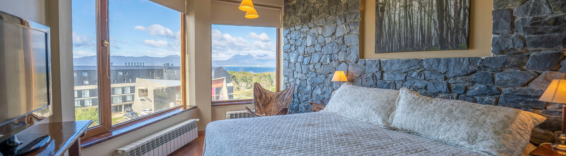 Superior-Doppelzimmer im Hotel Tierra de Leyendas in Ushuaia mit Natursteinwand, Kingsize-Bett und Panoramablick.