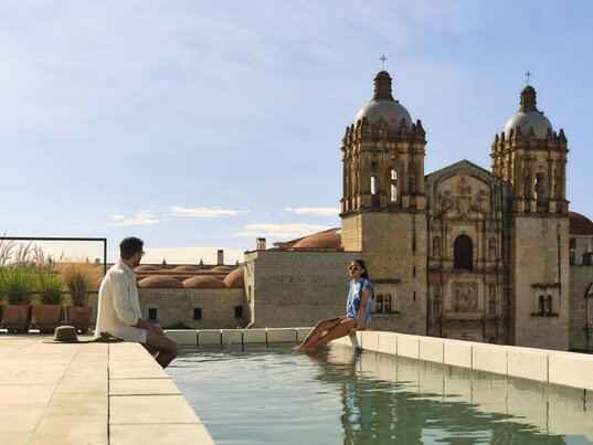 Paar am Rooftop-Pool des Hotel Otro mit Blick auf die Kathedrale Santo Domingo in Oaxaca, Mexiko.