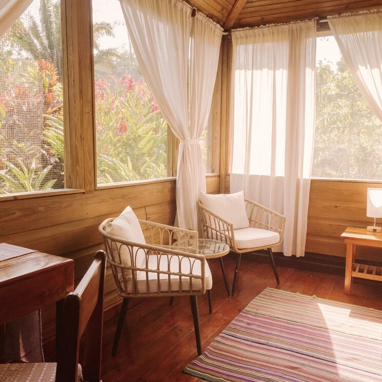 Sitzecke mit zwei Korbsesseln, Holztisch und bunten Teppichen in einer Cabana in San Ignacio, Belize.