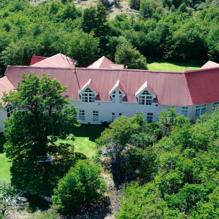 Luftaufnahme der Hosteria El Pilar mit rotem Dach, umgeben von dichten gruenen Waeldern in El Chalten, Argentinien.