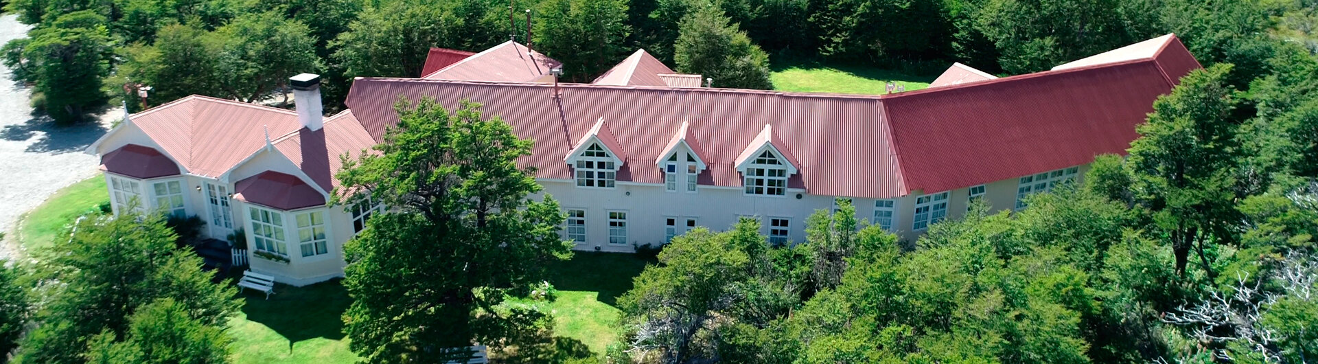 Luftaufnahme der Hosteria El Pilar mit rotem Dach, umgeben von dichten gruenen Waeldern in El Chalten, Argentinien.