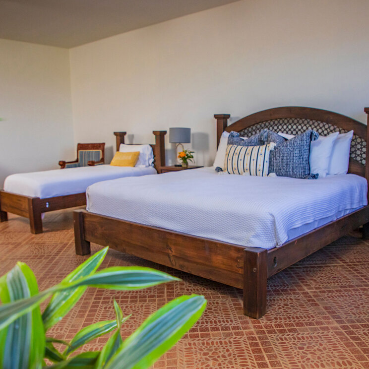 Hotelzimmer mit zwei dunklen Holzbetten, Terrakottaboden und einer gelben Kommode in Panama.