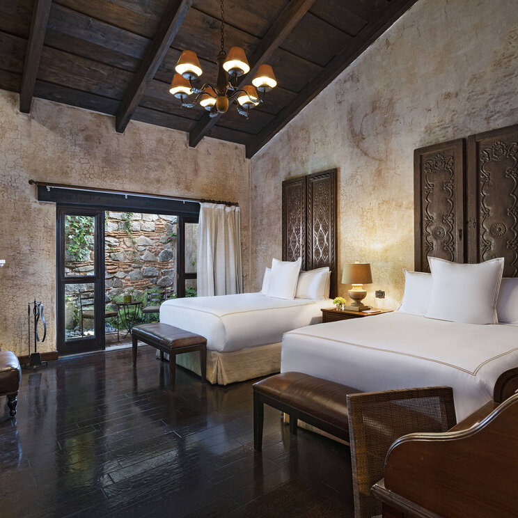 Stilvolles Zimmer im El Convento Boutique Hotel in Antigua, Guatemala, mit zwei Betten, Kamin, edlem Holzdekor und Blick in den Innenhof – luxuriöse Unterkunft im kolonialen Stil nahe der Altstadt.