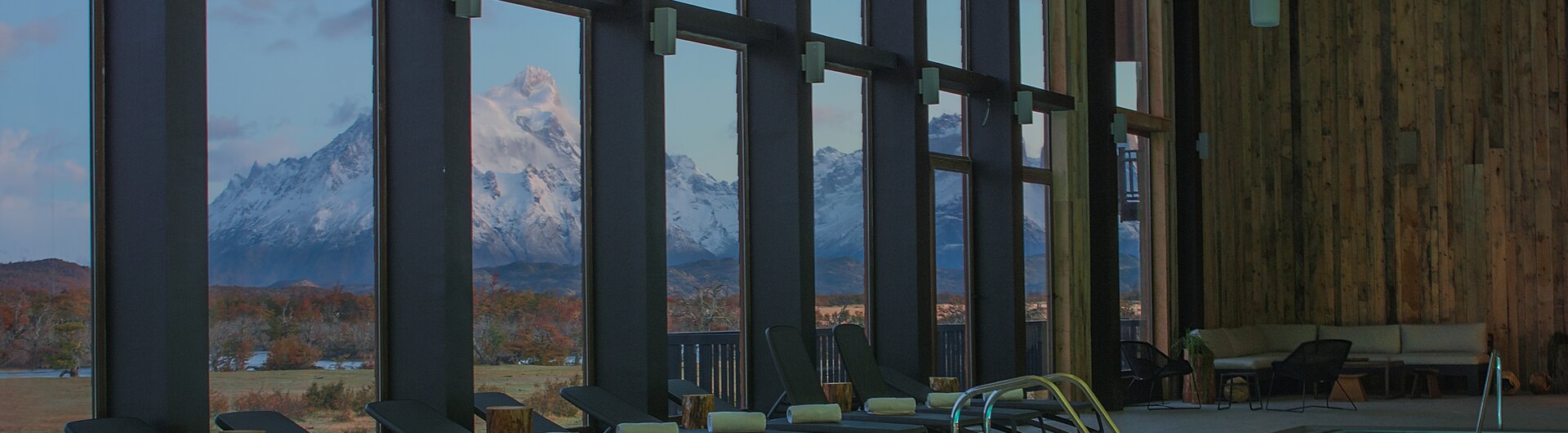 Innenansicht des Hallenbads im Hotel Rio Serrano mit Liegestühlen und Blick durch große Fenster auf die verschneiten Anden.
