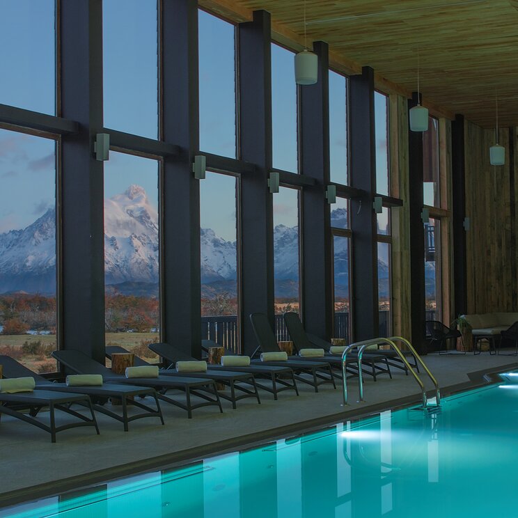 Innenansicht des Hallenbads im Hotel Rio Serrano mit Liegestühlen und Blick durch große Fenster auf die verschneiten Anden.