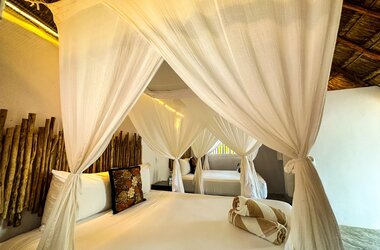 Doppelzimmer im Hotel Alito, Tulum, mit weißen Himmelbetten, Moskitonetzen und Wanddekor aus Holzstäben.