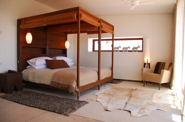 Doppelzimmer mit Himmelbett aus Holz, Webteppichen und Fenster mit Blick auf die Atacama-Landschaft in Chile.