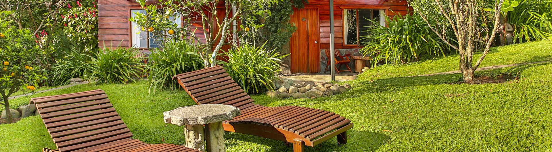 Sonnenliegen auf der Gartenwiese vor einem Holz-Bungalow der Arco Iris Lodge in Monteverde, Costa Rica.