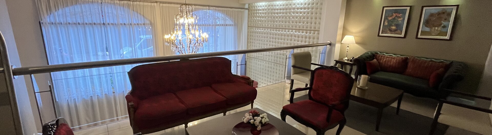 Hotel-Lobby in Lateinamerika auf einer Galerie mit roten Samtsesseln, Sofas, Holztischen und Kronleuchter vor Fenstern.