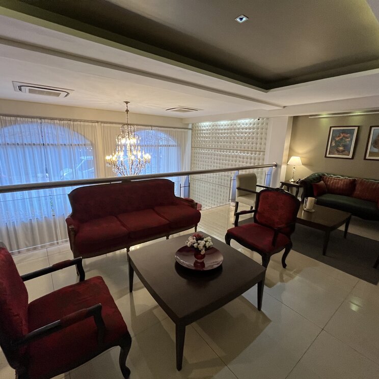 Hotel-Lobby in Lateinamerika auf einer Galerie mit roten Samtsesseln, Sofas, Holztischen und Kronleuchter vor Fenstern.