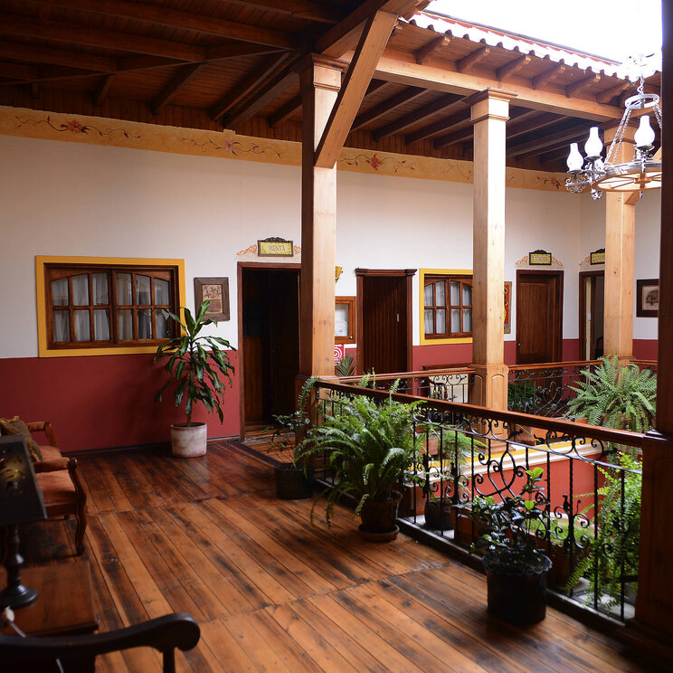 Oberer Innenhof im Hotel Santa Isabella in Riobamba, Ecuador, mit Holzboden, Pflanzen und Zugang zu den Gästezimmern rund um eine offene Galerie.