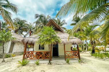 Traditioneller Bungalow mit Strohdach und Holzveranda zwischen Palmen im Hotel Alito in Tulum.