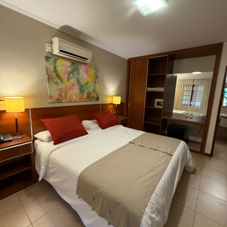 Doppelbett mit roten Kissen, Nachttischlampen, Klimaanlage und Holz-Einbauschrank mit Spiegel in Iguazu.
