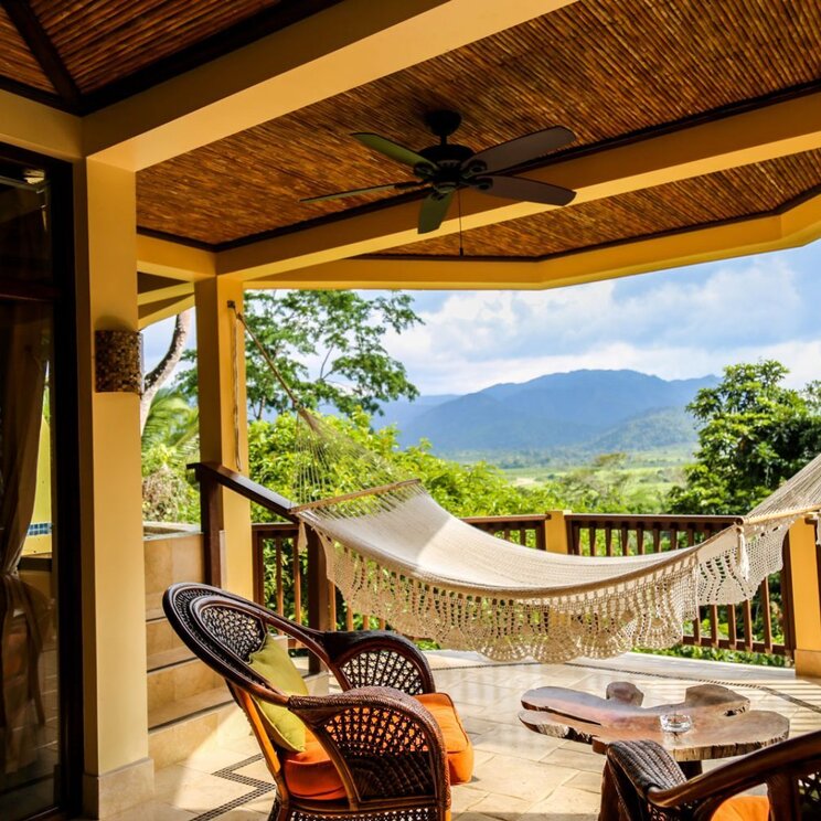 Überdachte Terrasse mit Hängematte, Korbstühlen und Blick auf die Berge von San Ignacio, Belize.