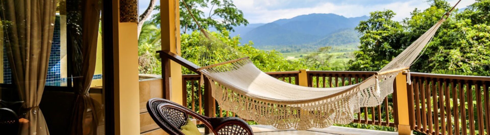 Überdachte Terrasse mit Hängematte, Korbstühlen und Blick auf die Berge von San Ignacio, Belize.