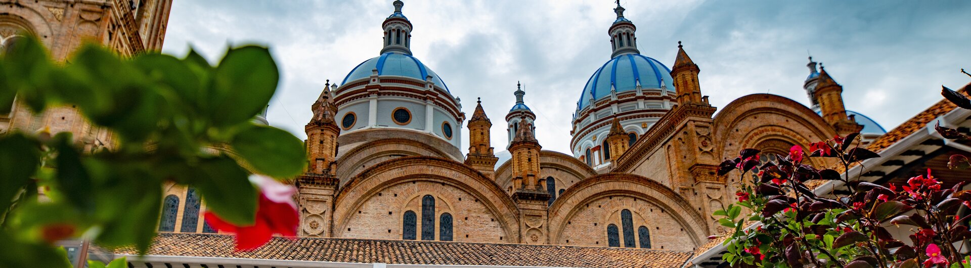 Kathedrale von Cuenca mit markanten blau-weißen Kuppeln und Backsteinfassade, gesehen von einem bepflanzten Innenhof.