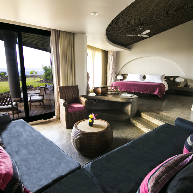 Helle Hotelsuite mit dunklen Sofas, runder Deckenvertiefung und Zugang zur Terrasse mit Blick auf den Ozean.