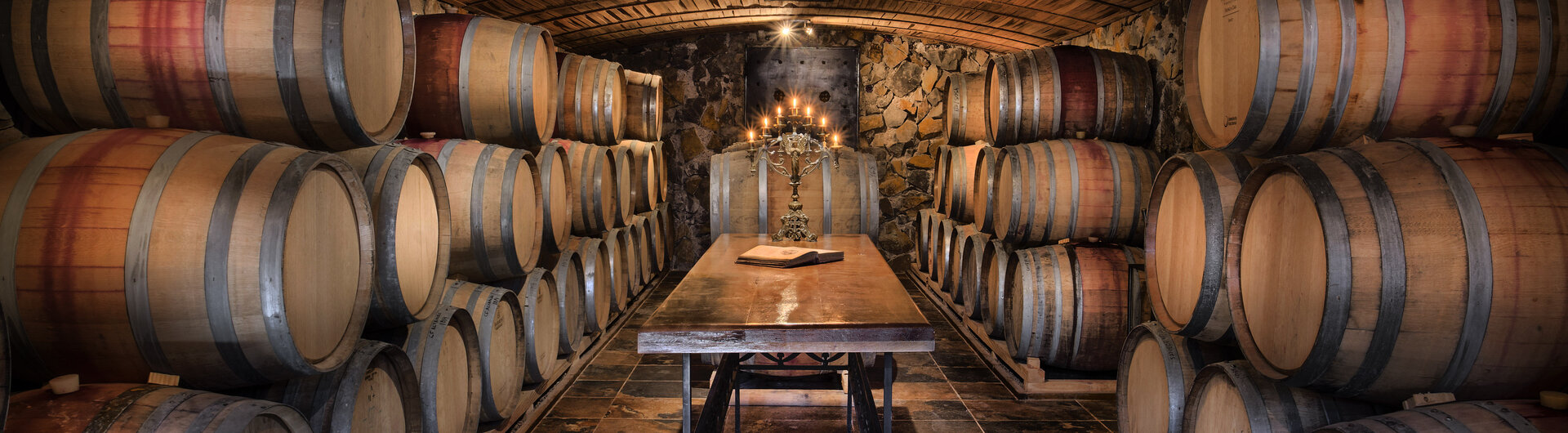 Stimmungsvoller Weinkeller mit gestapelten Eichenfässern und Verkostungstisch in der Bodega El Enemigo (Casa Vigil) in Mendoza, Argentinien