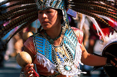Frau mit Feder-Kopfschmuck und indigener Kleidung bei musikalischer Zeremonie, Mexiko-Stadt