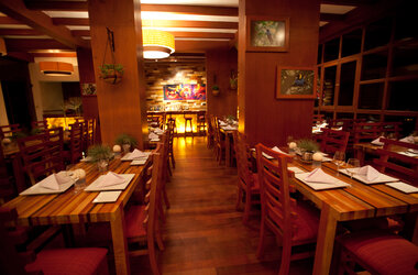 Innenansicht des Restaurants Manka mit gedeckten Holztischen, Holzsäulen und warmer Beleuchtung.