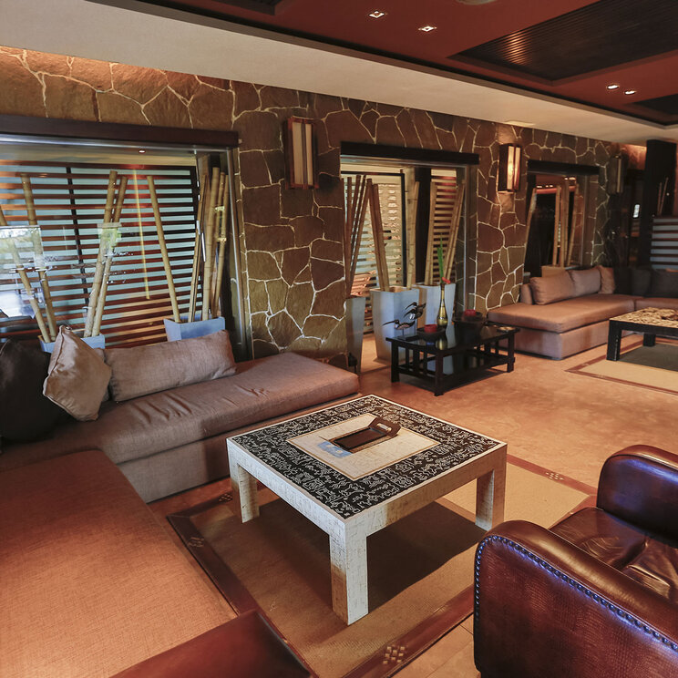 Hotellounge mit braunen Sofas, Ledersesseln und Couchtischen vor einer Steinwand im Imago Hotel & Spa in El Calafate.