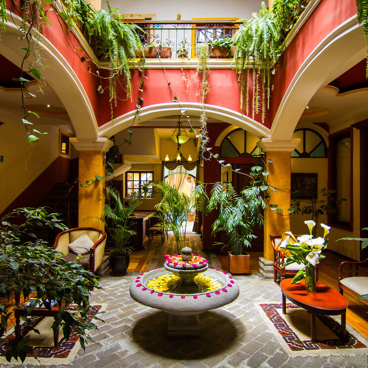 Oberer Innenhof im Hotel Santa Isabella in Riobamba, Ecuador, mit Holzboden, Pflanzen und Zugang zu den Gästezimmern rund um eine offene Galerie.