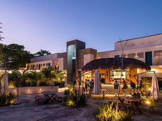 Beleuchteter Innenhof mit strohgedeckter Bar und Sitzbereichen am Abend im Hotel Waye, Valladolid.