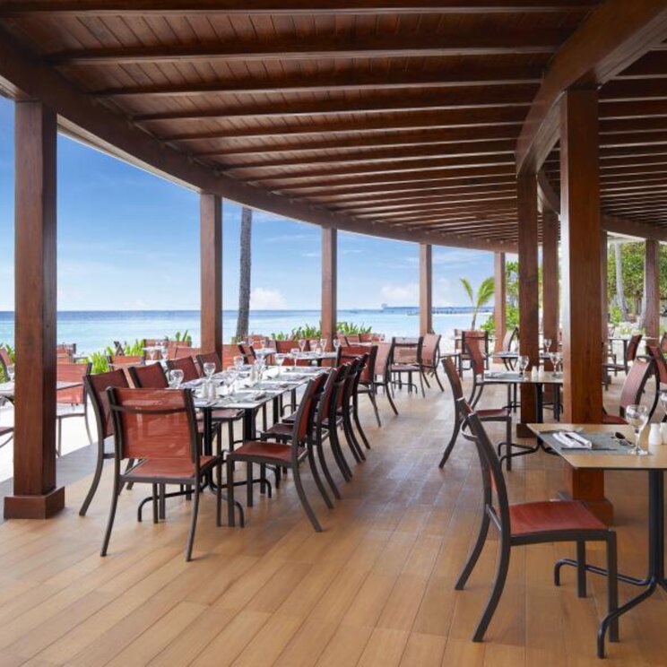 Überdachte Restaurant-Terrasse mit Holzboden, gedeckten Tischen und Blick auf das Meer in Punta Cana.