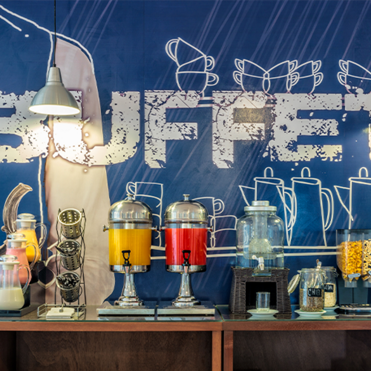 Frühstücksbuffet im LP Hotel Santa Cruz mit Säften, Müsli und Gebäck vor blauer Wandgrafik in Bolivien.